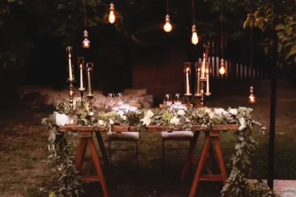 Tavolo da matrimonio all’aperto con candele e lampadine sospese, illuminazione calda e atmosfera intima serale
