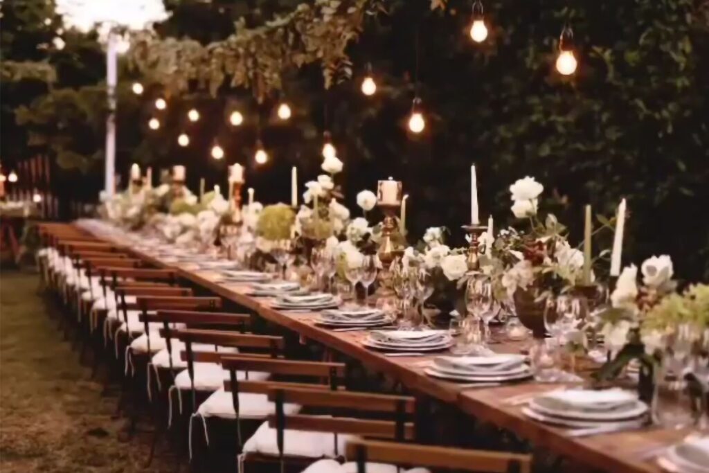 Tavolo imperiale per matrimonio all’aperto illuminato da lampadine a filamento, candele e composizioni floreali naturali